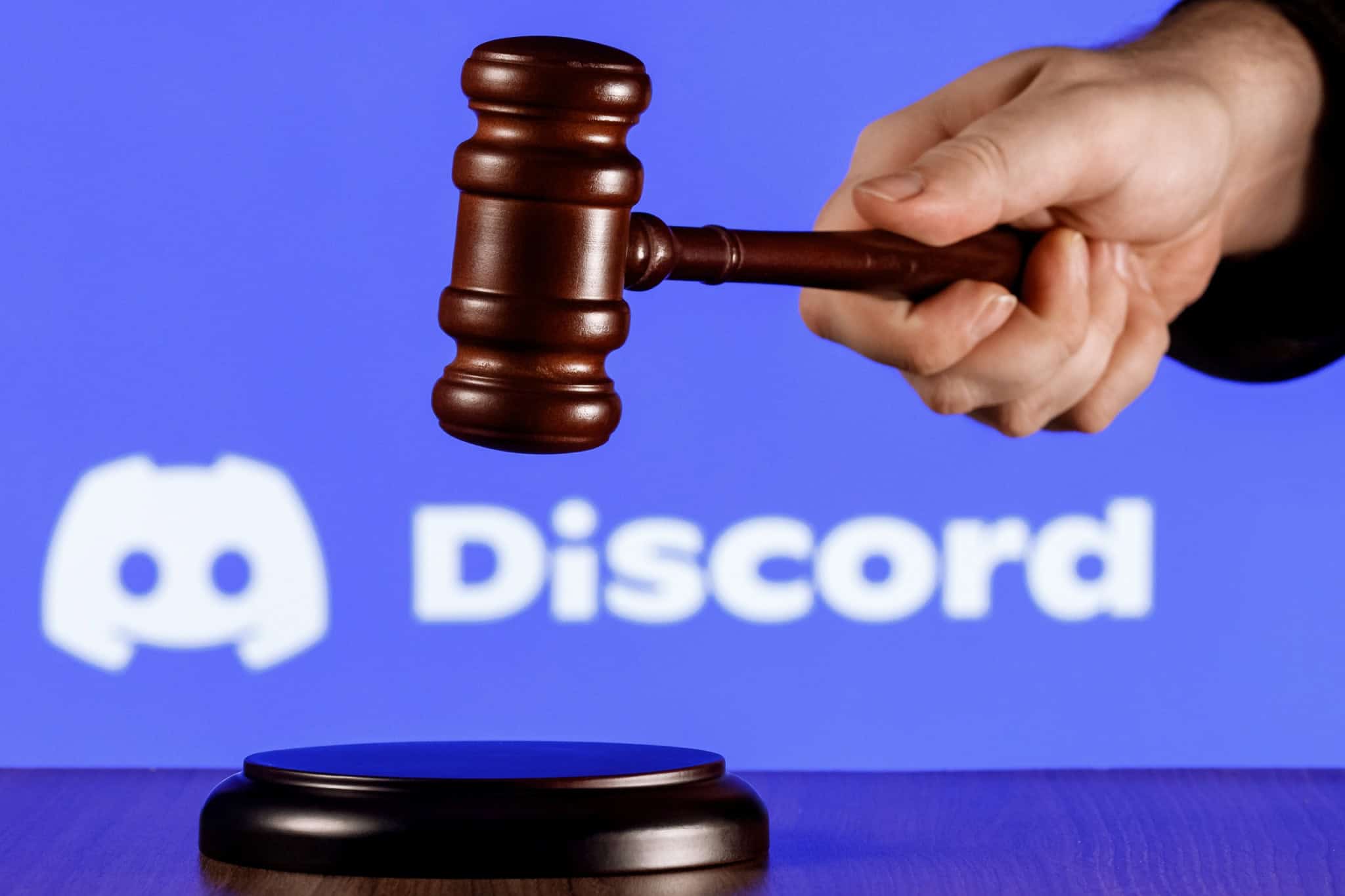 Ao fundo, logo do Discord; à frente, martelo de juiz na mão de uma pessoa
