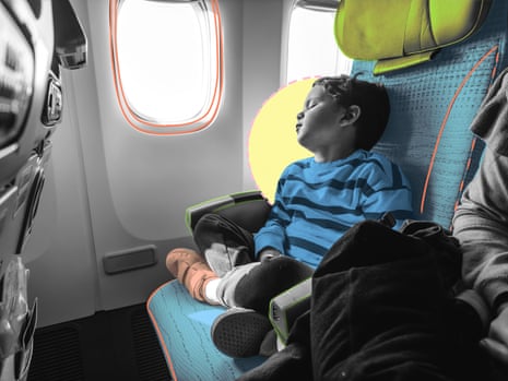 A young boy sleeps against an airplane seat, head tilted back, arms resting on his lap